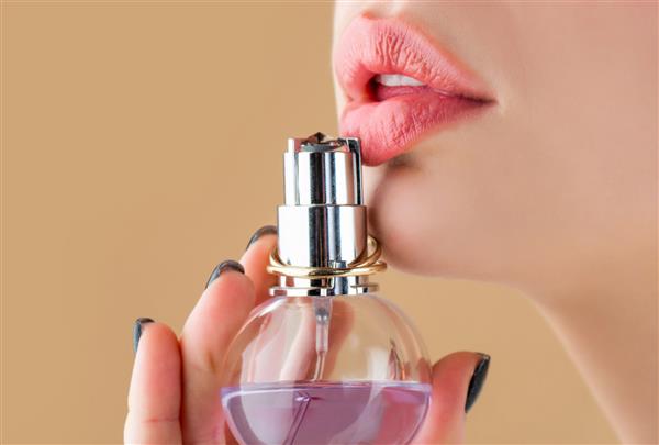 شیشه عطر زن لب های لب صورتی لب‌های نرم و پر از نزدیک با رژ لب قرمز تیره دختر زیبا با استفاده از عطر زن با شیشه عطر زن ارائه عطر عطر