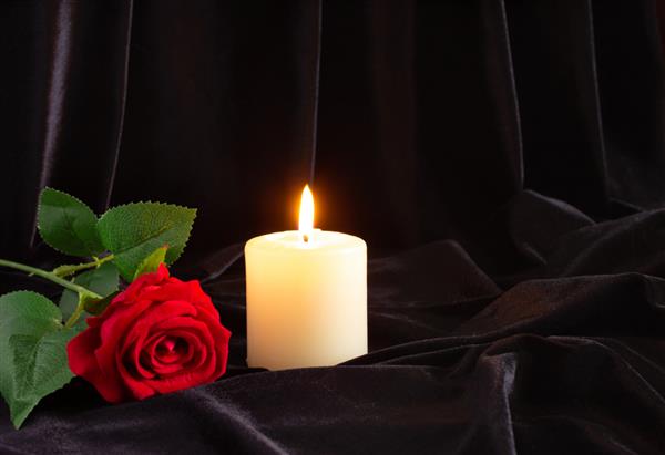 یک شمع سوزان و یک گل رز قرمز در زمینه سیاه مفهوم تعزیه عزاداری و تشییع جنازه