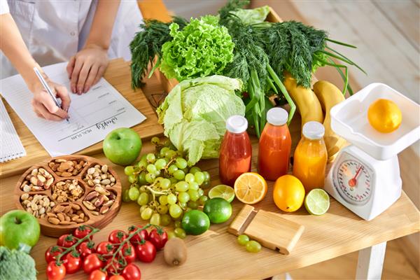 متخصص تغذیه جوان برنامه غذایی را می نویسد نمایی از بالا روی میز با محصولات مختلف سالم