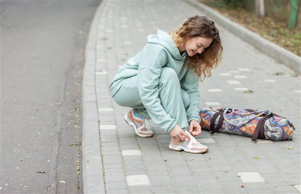 زن تناسب اندام در حال بستن بند کفش در فضای باز