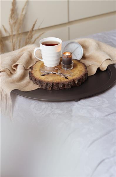 یک فنجان چای یک عینک یک شمع و یک ساعت نقره ای روی تخت مفهوم روتین صبحگاهی