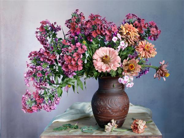 یک دسته گل زیبا با زینیا و فلوکس در گلدان با آب روی میز