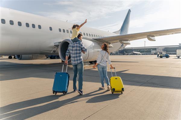نمای پشتی خانواده شاد که در نزدیکی یک هواپیمای بزرگ با دو چمدان در فضای باز ایستاده اند مفهوم سفر