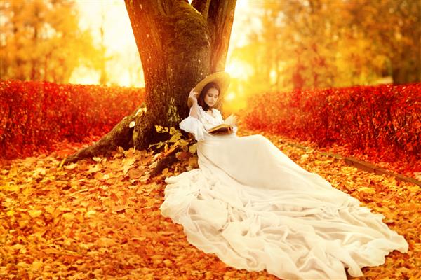 چشم انداز پاییزی زن رمانتیک به سبک ویکتوریایی در حال خواندن کتاب در پارک با برگ های افرا نارنجی پس زمینه رنگارنگ فصل پاییز روشن