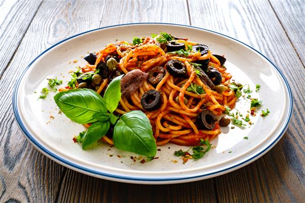 اسپاگتی پوتانسکا با سس گوجه فرنگی آنچوی فلفل قرمز کیپر و زیتون روی میز چوبی