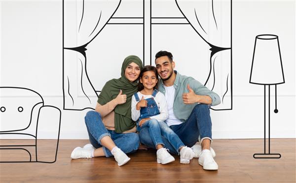مسکن خانوادگی خانواده خوشبخت عرب نشسته روی زمین نزدیک دیوار سفید با فضای داخلی ترسیم شده خانه جدید را تصور کنید سه نفر جوان خندان که شست را مانند اشاره نشان می دهند برنامه ریزی برای بازسازی در اتاق خالی