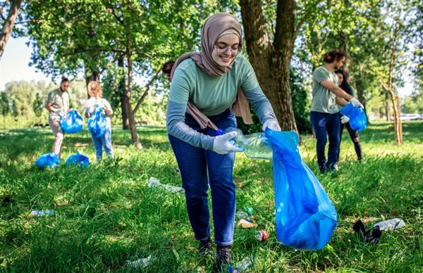 پرتره زن جوان مسلمان با کیسه زباله در حال تمیز کردن پارک شهر با دوستان