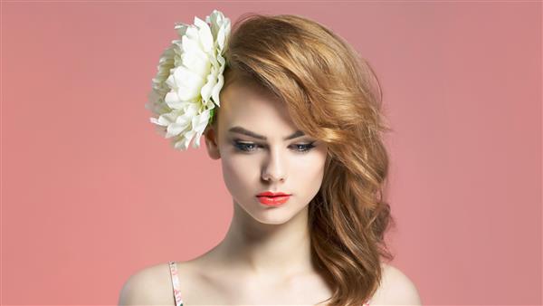 زن جوان بلوند زیبا با گل در مو دختر زیبایی بهار روی پس زمینه صورتی