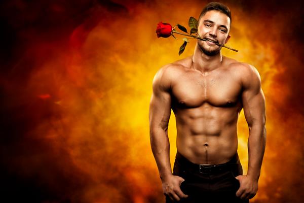 مرد بدنساز سکسی که گل رز را در دندان گرفته است مردان قوی روپوش گل را روی پس زمینه هنری شعله داغ ارائه می دهند مفهوم تعطیلات ولنتاین و عشق