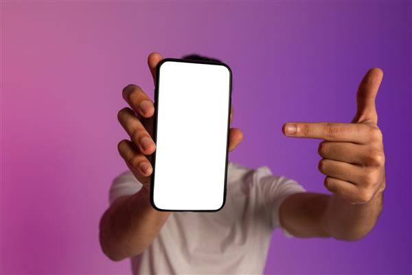مرد جوان نامشخصی که گوشی هوشمند را جلوی صورتش گرفته است به صفحه خالی اشاره می کند فضایی برای اپلیکیشن موبایل یا وب سایت ارائه می دهد ماکت تبلیغات آنلاین را در نور نئون نشان می دهد فوکوس انتخابی