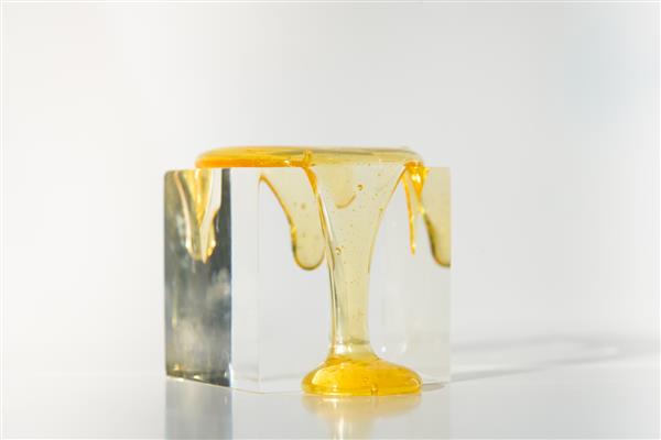نمای نزدیک از ترکیب هنری زیبایی با عسل مایع روی مکعب شیشه ای در پس زمینه روشن ترکیب انتزاعی درباره عسل طبیعی در زندگی افراد