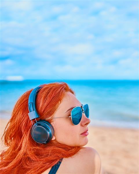 زن مو قرمز در حال گوش دادن به موسیقی در ساحل زن سکسی در حال گوش دادن به موسیقی در ساحل مفهوم تعطیلات در اقیانوس آرام باشید