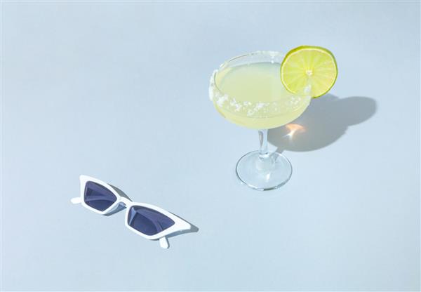 صحنه آفتابی مرسوم با لیوان کوکتل و عینک آفتابی سفید مفهوم سفر تابستانی ایده مینیمال مهمانی ساحلی