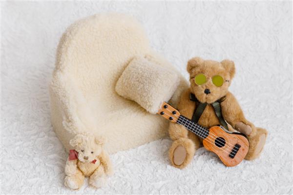 با مبل خرس عروسکی با عینک آفتابی و گیتار برای نوزاد در پس‌زمینه سفید عکس بگیرید منطقه عکس برای یک جلسه عکس از نوزادان راه اندازی آماده برای عکاسی نوزاد و عکاسی نوزاد