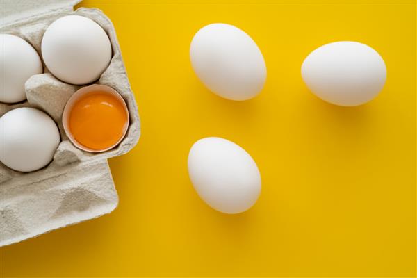 نمای بالای تخم مرغ و زرده در پوسته در بسته بندی روی زمینه زرد