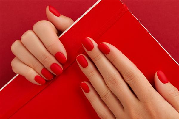دست زن با مانیکور نگه داشتن دفترچه یادداشت طراحی ناخن قرمز مات