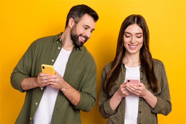 عکس زوج مثبت گذراندن اوقات فراغت در گوشی های هوشمند در حال گشت و گذار در رسانه های اجتماعی جدا شده بر روی پس زمینه زرد رنگ