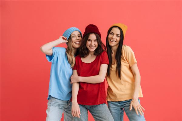 سه دختر جوان شاد در حال لبخند زدن و ژست گرفتن در مقابل دوربین جدا شده روی پس زمینه قرمز