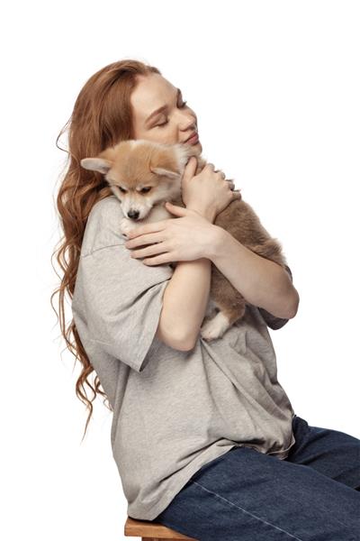 آغوش دختر جوان مو قرمز شاد با موهای فرفری بلند که توله سگ کوچولوی ناز سگ کورگی جدا شده در پس زمینه سفید را در آغوش گرفته است مفهوم جوانی زیبایی زندگی فضای تبلیغاتی را کپی کنید