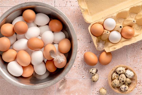 تخم مرغ در کاسه فلزی در زمینه بژ نمای بالای تخم مرغ قهوه ای خام و تخم مرغ سفید در جعبه تخم مرغ باز