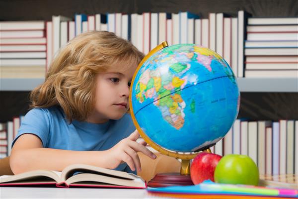 بچه مدرسه ای در کتابخانه مدرسه ابتدایی به کره زمین نگاه می کند کودک از دبستان شاگرد برو درس بخون یادگیری دانش آموز باهوش مفهوم مطالعه دانش و آموزش کودکان