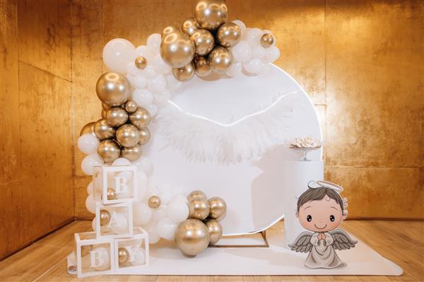 طاق لاکچری برای تولد کودک در رستوران منطقه عکس با بادکنک های طلایی و بال های سفید فرشته با حروف منطقه عکس برای جشن