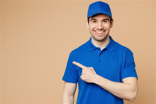 مرد کارمند پسر تحویل مبارک با لباس کار یکنواخت تی شرت کلاه آبی به عنوان پیک فروشنده که انگشت اشاره را به کناری نشان می دهد روی ناحیه ایزوله شده روی پس زمینه بژ روشن ساده کار می کند مفهوم خدمات