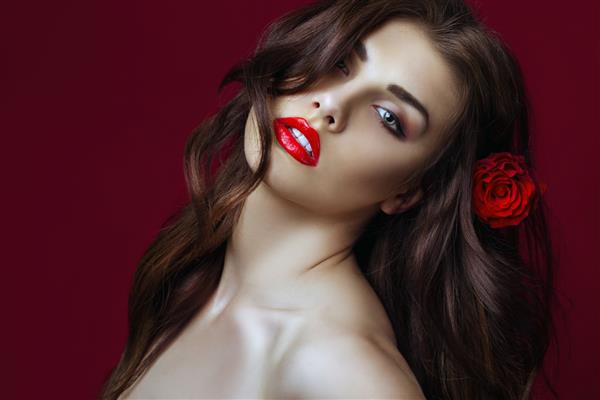 زن مد سکسی زیبا با گل رز در موهایش آرایش با لب های قرمز موهای بلند عالی و رز قرمز دختر زیبای ایتالیایی شور نزدیک فضای کپی