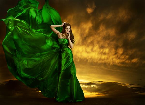 لباس مد زنانه که روی باد بال می زند پرتره دختر زیبا مدل ژست مدل با پارچه لباس مجلسی ابریشمی سبز پارچه تکان در آسمان شب