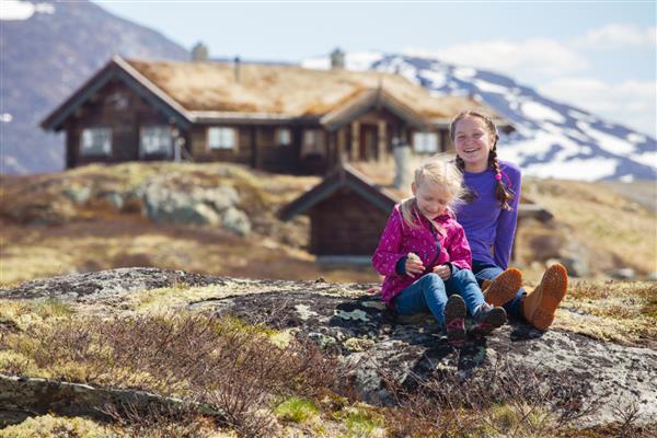 دختر کوهنوردی که روی پس‌زمینه خانه‌های چوبی سنتی قدیمی در تین نروژ نشسته است