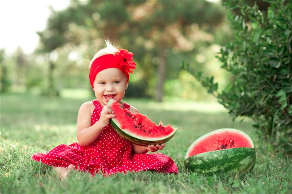 دختر بچه 1 تا 2 ساله خندان در حال خوردن هندوانه در فضای باز نگاه کردن به دوربین دوران کودکی