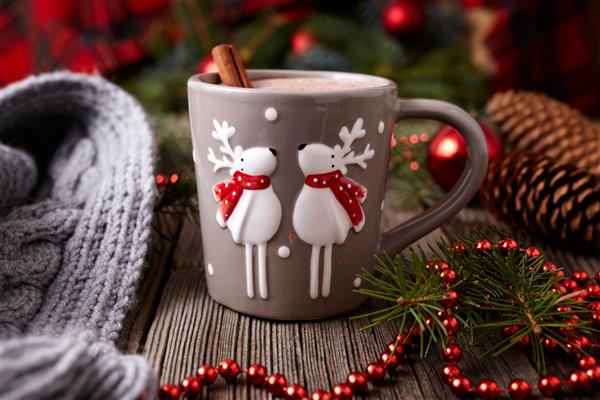فنجان شکلات داغ یا کاکائو با دو گوزن زیبا و دارچین در قاب تزئینات درخت سال نو در زمینه میز چوبی قدیمی دستور پخت جشن سنتی خانگی سبک روستیک