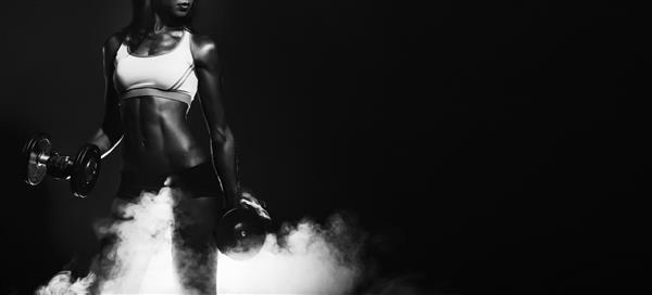 زن ورزشکار دختر ورزشکار با دمبل عکاسی استودیویی اثرات دود دختر سالم ورزشکار با دمبل های بزرگ در دستانش عضلات در حال کار ورزشخشک کاری عضلات سیاه و سفید