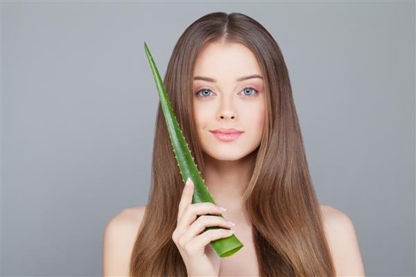 زنی با پوست شفاف و موهای بلند و سالم که برگ سبز آلوئه را در دست گرفته است
