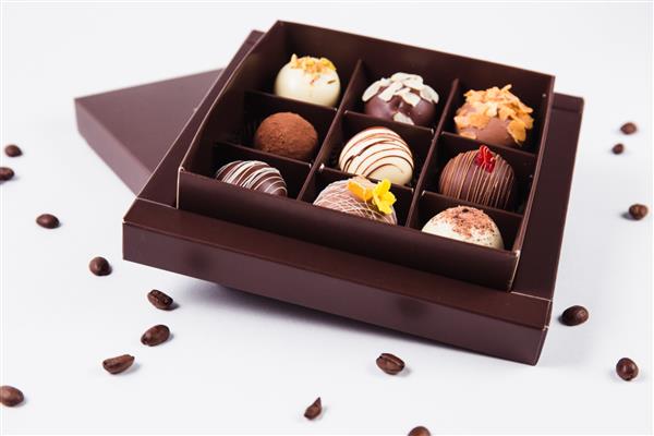 شکلات های دست ساز در یک جعبه مربع و دانه های قهوه در اطراف