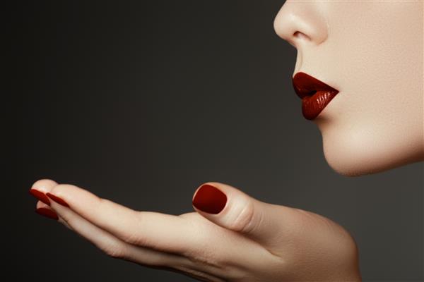 زن جوان زیبا در حال بوسه از دست خود مدلی با لب های قرمز تیره عالی و ناخن های قرمز مانیکور شده
