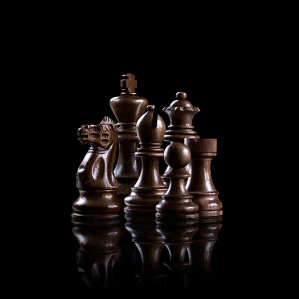 مفهوم استراتژی و رهبری؛ فیگورهای چوبی سیاه شطرنج که در کنار هم به عنوان یک خانواده آماده برای بازی در پس زمینه تاریک ایستاده اند