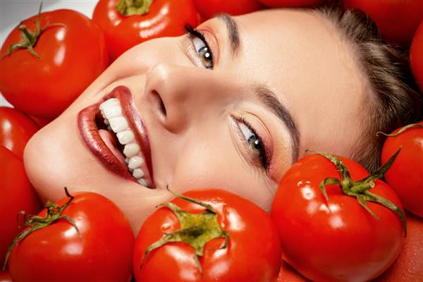 پرتره نزدیک از یک زن خندان زیبا در میان گوجه فرنگی مفهوم تغذیه سالم لوازم آرایش لوازم آرایش