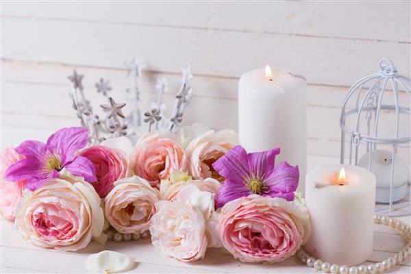 گل رز صورتی و گل های کلماتیس بنفش شمع ها در زمینه چوبی سفید تمرکز انتخابی مکانی برای متن