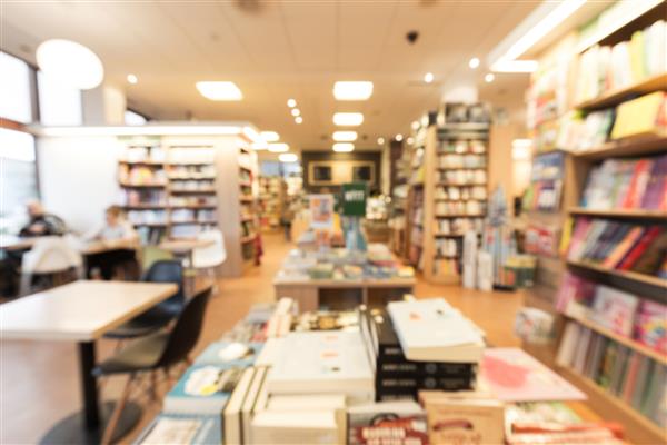عکس خارج از فوکوس از داخل یک کتابفروشی با کافه کتاب در قفسه ها و روی میزها مشتریان در حال خواندن مجلات و نوشیدن قهوه در سمت چپ