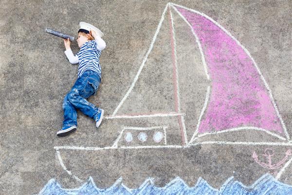 پسر کوچک ناز در حال قایقرانی در کشتی یا قایق نقاشی با گچ اوقات فراغت خلاقانه برای کودکان در فضای باز در تابستان