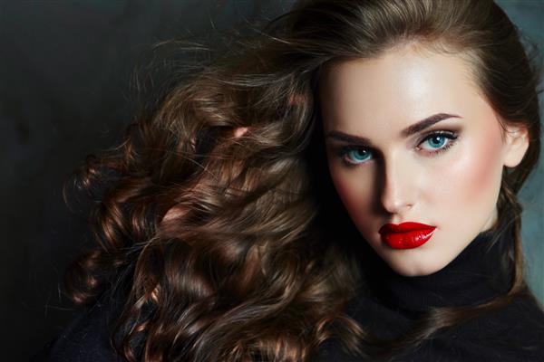 دختر جوان و زیبای خودنمایی با موهای براق مواج مجلل به قاب نگاه می کند موهای قهوه ای چشمان آبی لب های قرمز بزرگ یک پرتره بزرگ مد زیبایی مراقبت سلامتی سالن