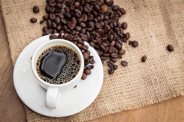 قهوه سیاه در فنجان با دانه روی گونی تفنگدار با میز چوبی نمای بالا