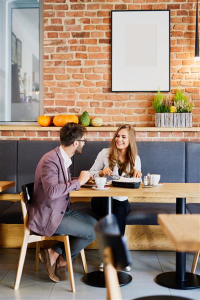 زن و شوهر جوان قبل از رفتن به سر کار در یک کافه تریا در حال گفتگو و خوردن صبحانه هستند