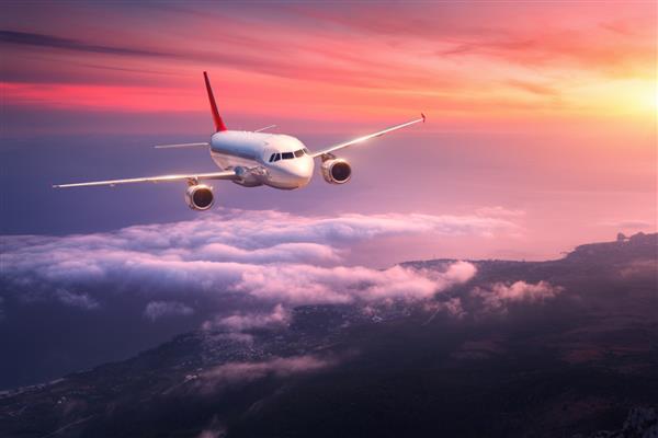 هواپیمای مسافربری منظره ای با هواپیمای سفید بزرگ در آسمان قرمز بر فراز ابرها و دریا در غروب رنگارنگ در حال پرواز است هواپیمای مسافربری در غروب در حال فرود است سفر کاری هواپیمای تجاریسفر
