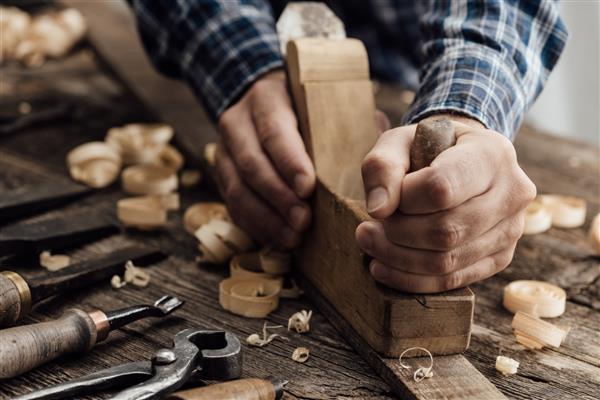 نجار که در کارگاه خود مشغول به کار است او در حال صاف کردن یک تخته چوبی با استفاده از دستگاه رنده نجاری نجاری نجاری و مفهوم صنایع دستی است