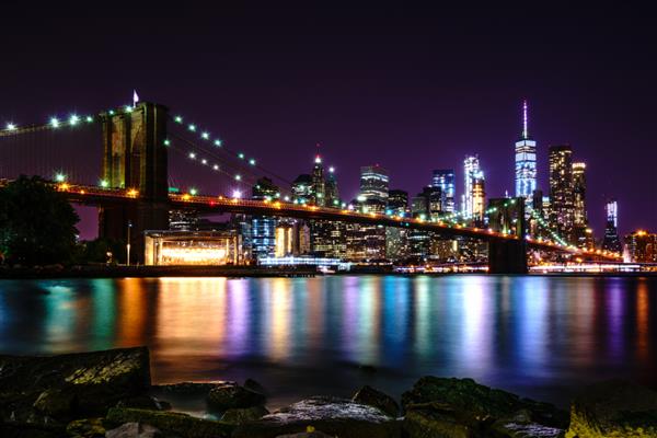 پل بروکلین در شب با انعکاس آب خط افق شهر نیویورک