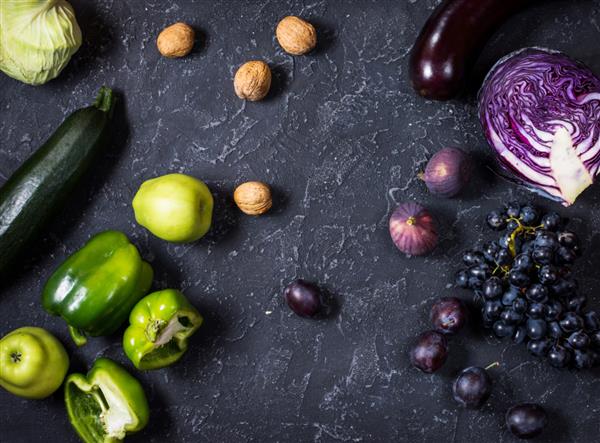 سبزیجات و میوه های رنگی سبز و بنفش خام ارگانیک تازه در زمینه سنگی تیره