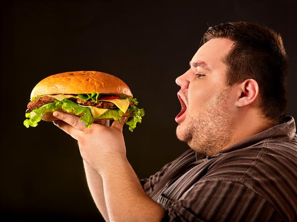 شکست رژیم غذایی مرد چاق در حال خوردن همبرگر فست فود صبحانه برای افراد دارای اضافه وزن که با خوردن همبرگر بزرگ غذای سالم را خراب کرده اند وعده های غذایی ناسالم منجر به چاقی می شود پختن همبرگر در خانه