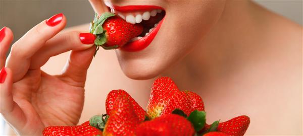 زن جوان در حال خوردن توت فرنگی رسیده قرمز از نزدیک عکس استودیویی